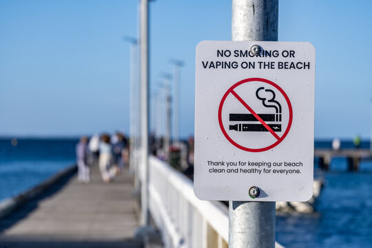 No smoking and vaping sign displayed on a public pier at a coastal beach in Australia. Public space regulation signage supporting environmental protection, health policy, and shared use management