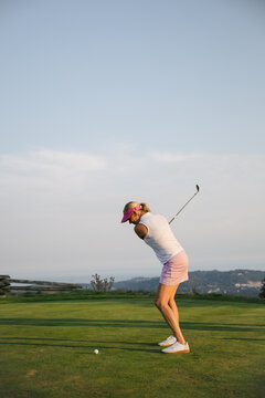 Candid golf moment: woman in pink visor teeing off on course