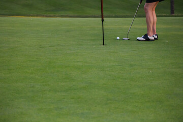 Candid golfer lining up a putt on the green, legs and club visible