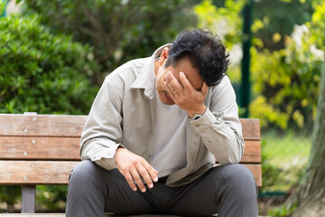 ベンチを座りながら落ち込んでいるミドル男性　ライフスタイルイメージ