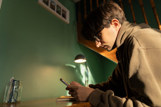 Young Male Student getting distracted by the Phone while studying home