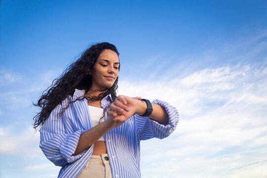 Low angle view of a woman using smartwatch against blue sky