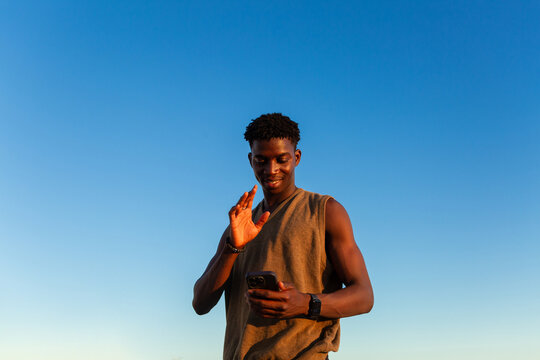 Young Man Waves at Smartphone Under Blue Sky
