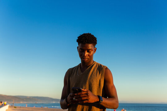 Young Man Using Smartphone on a Beach at golden hour