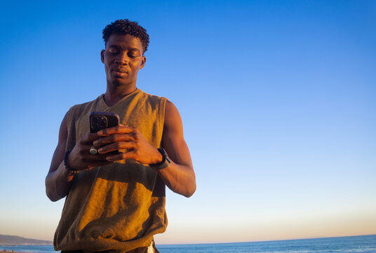 Young Man Using His Phone by the Beach at Sunset