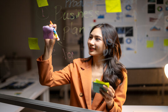 Asian businesswoman brainstorming new business plan on glass board - Powered by Adobe