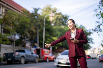 Asian businesswoman hailing taxi with smartphone on city street