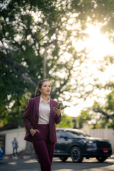 Asian businesswoman walking outdoors holding phone in suit