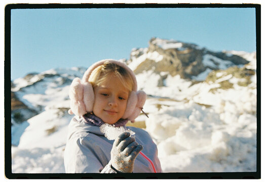 Girl with pink earmuffs holding ice in snowy mountains