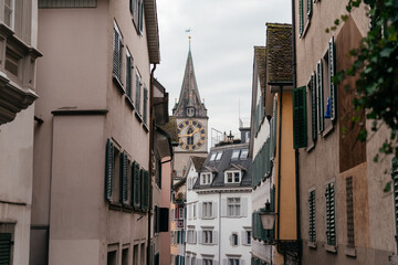 Fototapeta premium A panoramic cityscape of Zurich featuring historic church towers and rooftops under a cloudy sky. The image captures the charm of Switzerland old town with mountains in the background.