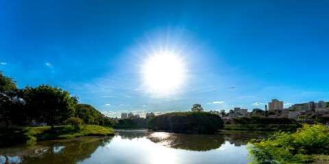 Fototapeta premium Urban lake with sunlight reflection and green park under blue sky