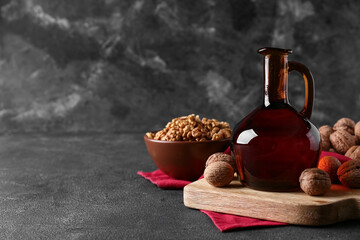 Tasty walnuts and jug of oil on grey grunge background