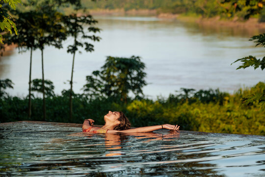 Woman Relaxing in Infinity Pool Overlooking Lush Riverside Landscape