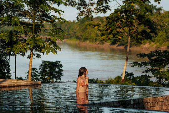 Woman Relaxing in Infinity Pool Overlooking Lush Riverside Landscape