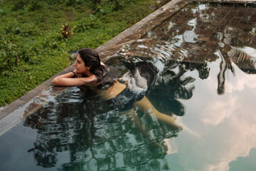 Woman relaxing in infinity pool surrounded by tropical forest