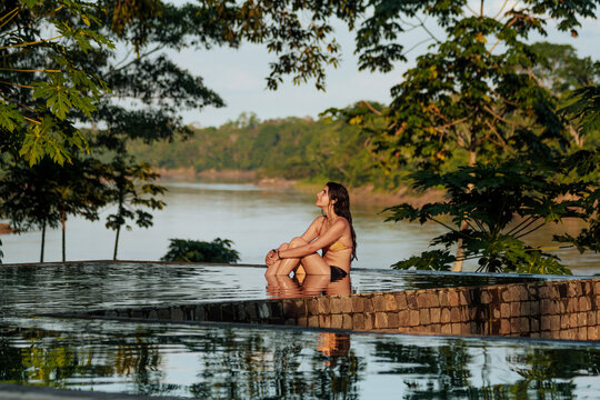 Woman Relaxing in Infinity Pool Overlooking Lush Riverside Landscape