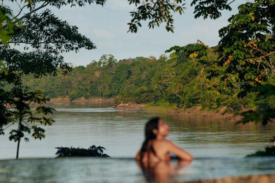 Woman Relaxing in Infinity Pool Overlooking Lush Riverside Landscape