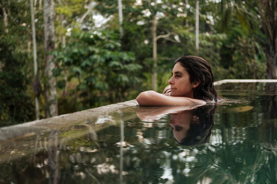Woman relaxing in infinity pool surrounded by tropical forest