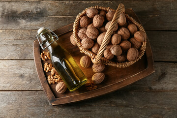 Bottle of fresh walnut oil and wicker basket with nuts on wooden background