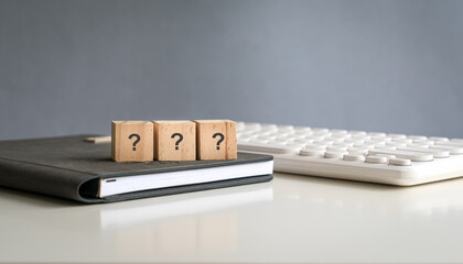 Question marks on wooden square blocks, on top of a book and next to a computer keyboard. 