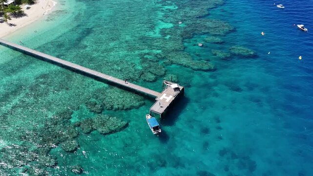 aerial drone view of the long wooden pier at Mala Mala Beach Club, Fiji. Crystal clear turquoise waters and vibrant coral reefs surround this private island paradise.