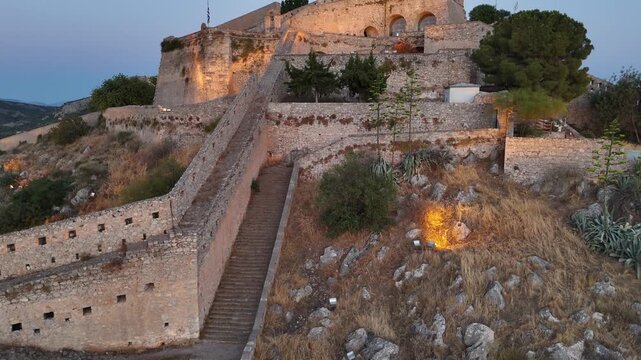 Peloponnese,Nafplion,Aerial view backwards and descending slowly from top of beautifully illuminated Palamidi Fortress towards bottom during sunset.