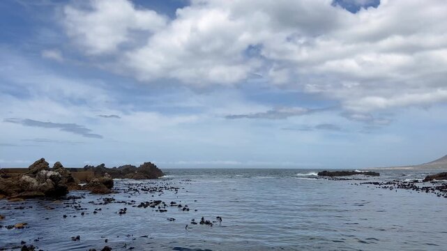 Waves crash on the distant rocks and push in and pull back out in a small harbor.