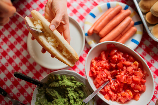Hands Assembling a Chilean Completo Hot Dog at Home