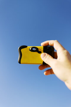 Hand Holding a Yellow Camera Against a Clear Blue Sky