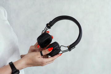 Naklejka premium Female hands with red manicure holding black wireless headphones against a light background. Music, audio technology, modern lifestyle and listening concept.