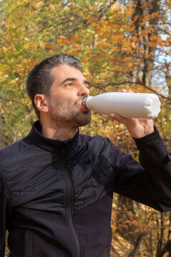 Man with water bottle in hand and autumn forest in the background