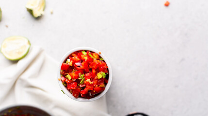 overhead view of salsa in a white bowl, top view of pico de gallo in a white ramekin on a grey countertop