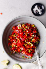 overhead view of salsa in a grey bowl, top view of ingredients for making pico de gallo in a grey bowl