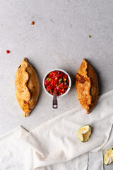 Overhead view of baked empanadas with pico de gallo on a grey cement countertop, top view of empanadas and salsa, bolivian salte&ntilde;a with chopped tomato sauce