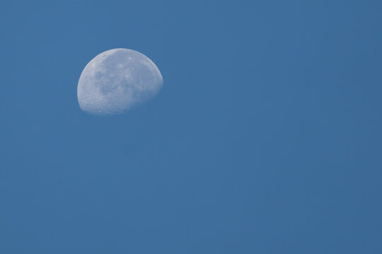 Daytime moon phase with visible craters against a solid blue background, perfect for use as a minimal wallpaper.