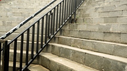 Detailed view of a sturdy black steel handrail installed on grey stone steps. This image highlights public safety infrastructure, urban architectural design, and durable outdoor materials.