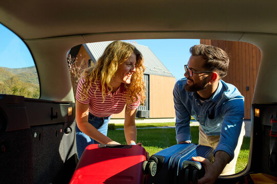 Couple is unloading their suitcases from a car