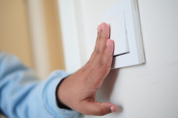 A child hand is pressing a light switch on a wall inside a room