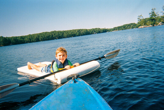 Child lies on floatie attached to kayak on the lake