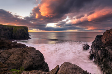 Obraz premium Dramatic Coastal Sunset Over Rugged Cliffs With Pink Clouds and Calm Sea