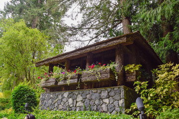 Rustic log cabin structure decorated with colorful flower boxes in a botanical garden.