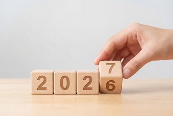 Hand turning wooden cube block to change year from 2026 to 2027 on table