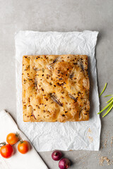 overhead view of onion and scallion focaccia on parchment paper, top view of airy bubbly onion focaccia on a cement countertop