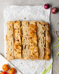 overhead view of slices of onion and scallion focaccia on parchment paper, top view of airy bubbly onion focaccia on a cement countertop