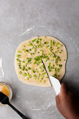 Overhead view of scallions on chinese pancake dough on grey countertop, process of making homemade scallion pancakes or cong you bing