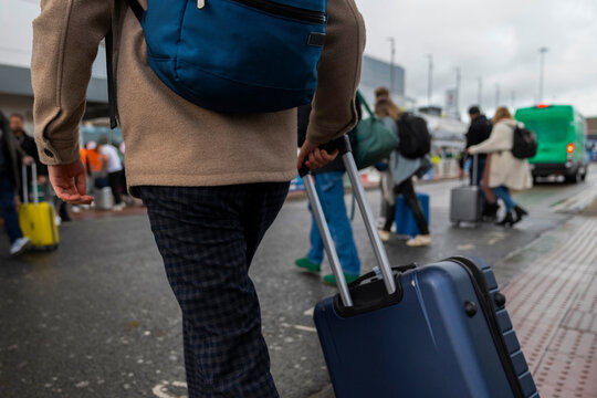 Anonymous Man With Luggage Crosses Streets Outside Airport Terminal