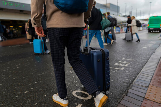 Anonymous Man With Luggage Crosses Streets Outside Airport Terminal