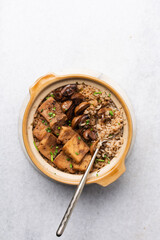 Overhead view vegan claypot rice with pan fried tofu, mushrooms and scallions, top view of crispy rice in a donabe on a marble countertop