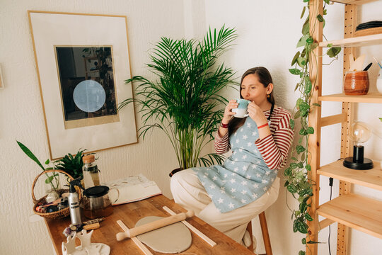 Woman sipping tea in calm pottery studio at home