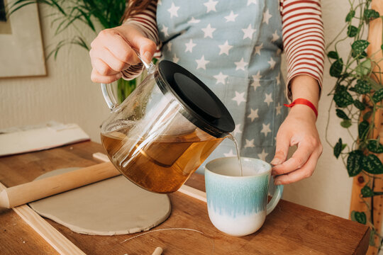 Pouring herbal tea in ceramic cup beside clay work